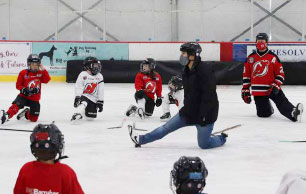 hockey instructor showing kids in NJ Devils hockey jerseys stretching exercises on ice