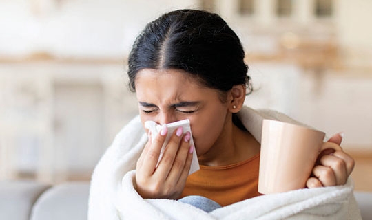 woman with coffee cup and tissue over nose