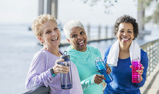 3 women drinking water together and smiling, after exercising