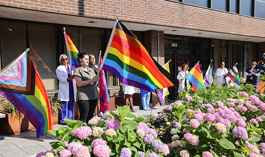 NBI staff holding up different pride flags out in front of the hospital building
