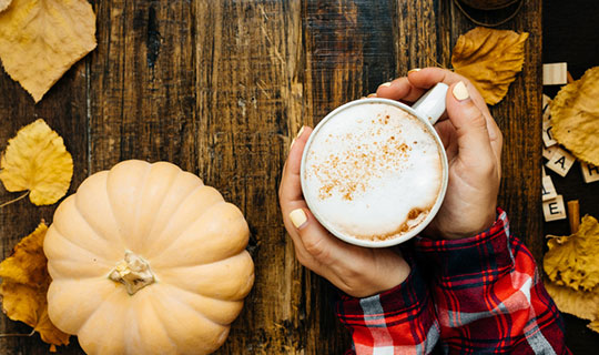 overhead photo of woman holding pumpkin spice latte in a coffee cup next to a pumpkin