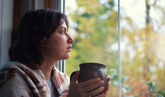 woman sitting and staring out of her window with a coffee cup in her hands