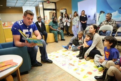 Sickle Cell Anemia Center - man in football jersey reading to kids sitting on a blanket on the floor