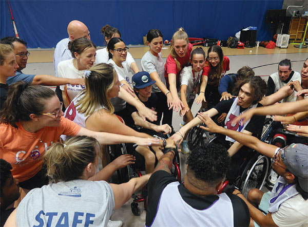 group of teens - some standing, some in wheelchairs - in a circle with their hands pointed to the center of the circle