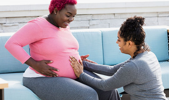 pregnant woman sitting on a couch with a doula talking with her